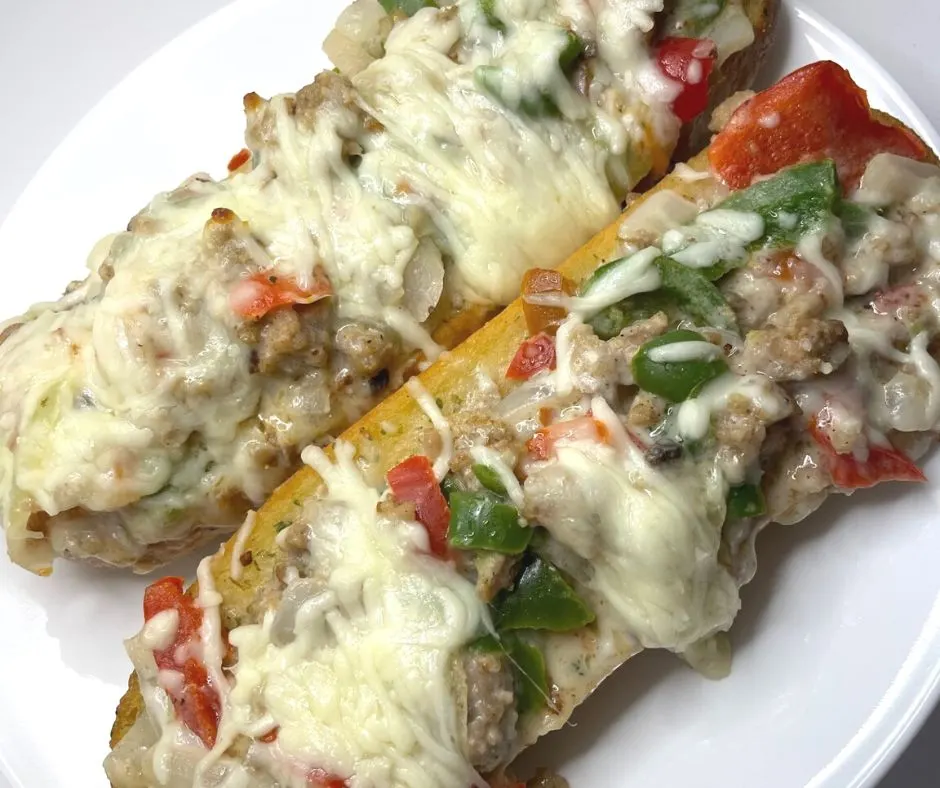 two large garlic loaf halves smothered in sausage, green and red peppers, onions, and mozzarella cheese on white plate