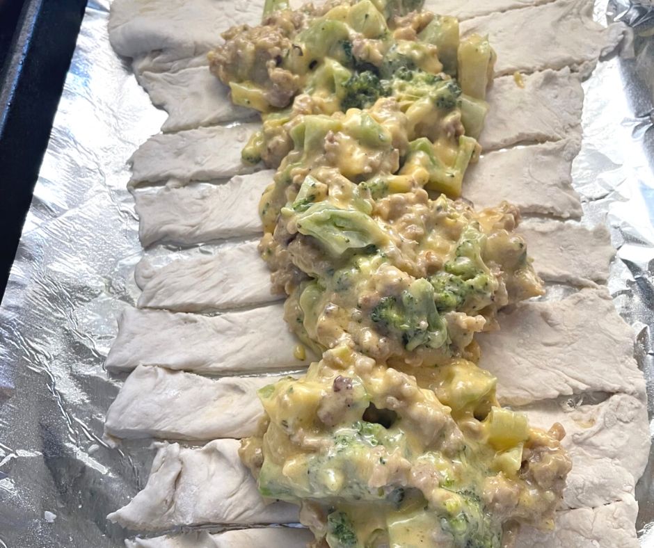 Uncooked dough with slits on sides, filled with sausage, broccoli, cheddar sauce before going into oven