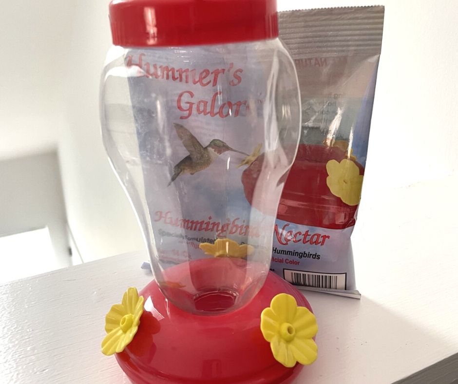 plastic hummingbird feeder with yellow flowers on bottom, nectar package behind it