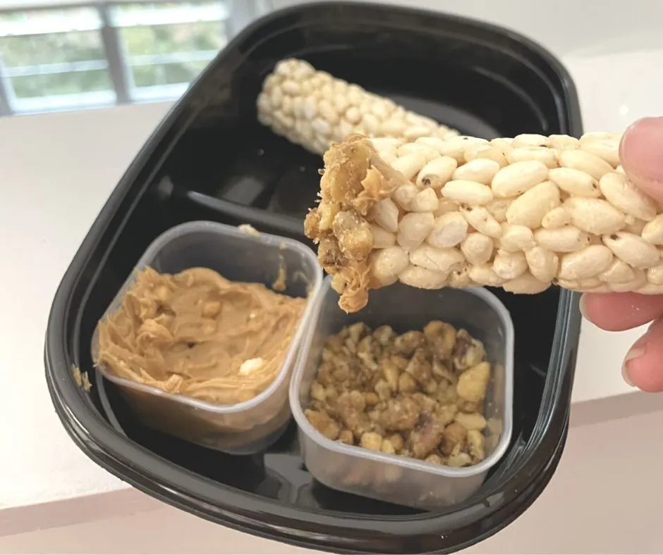 black snack container and two smaller containers all from Dollar Tree with rice sticks to dip into walnuts and peanut butter