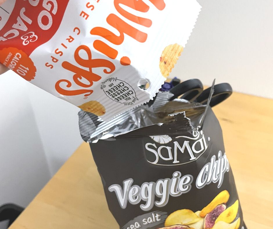 person pouring bag of Whisps into bag of veggie chips at desk