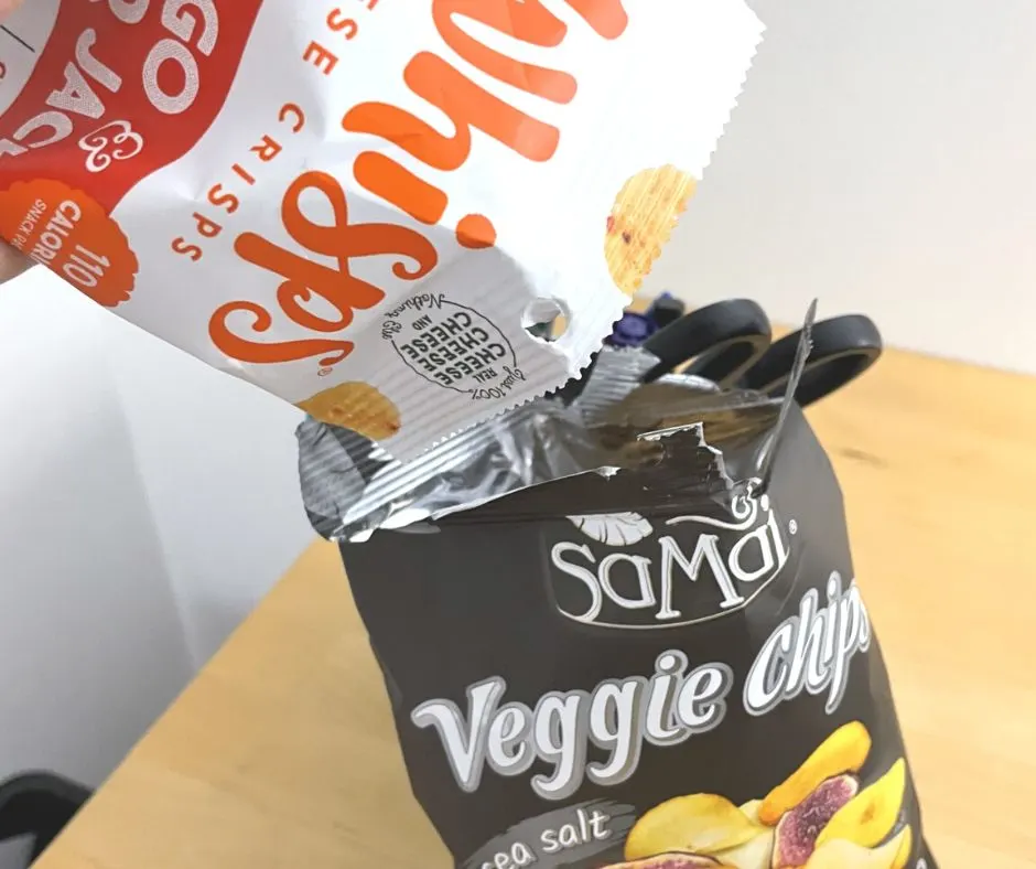 person pouring bag of Whisps into bag of veggie chips at desk