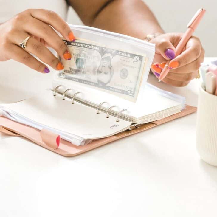 woman's hands with filled A6 binder cash envelopes and a pen at desk