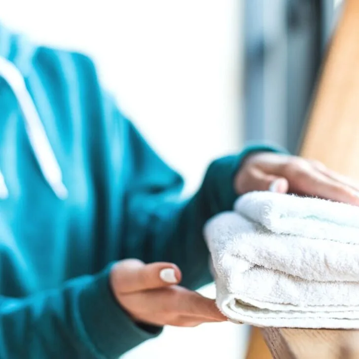 woman in blue hooded shirt folding white towels on wooden ladder