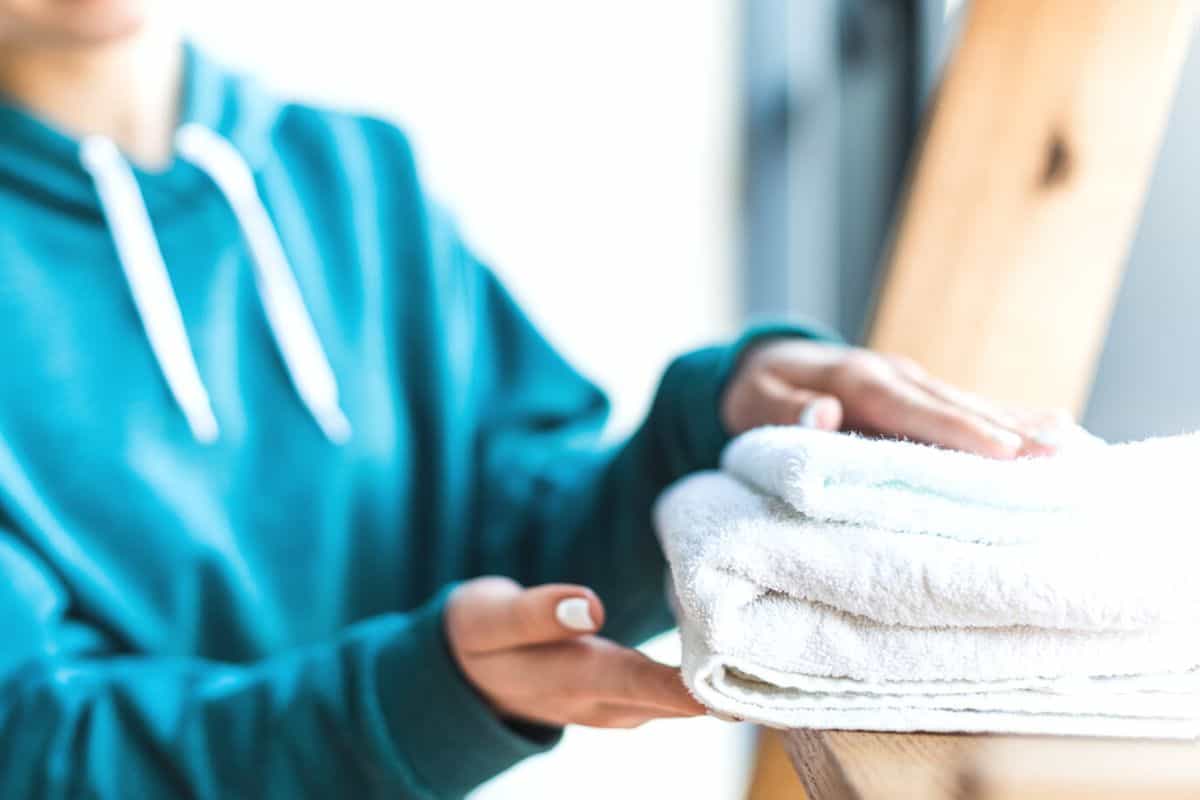 woman in blue hooded shirt folding white towels on wooden ladder