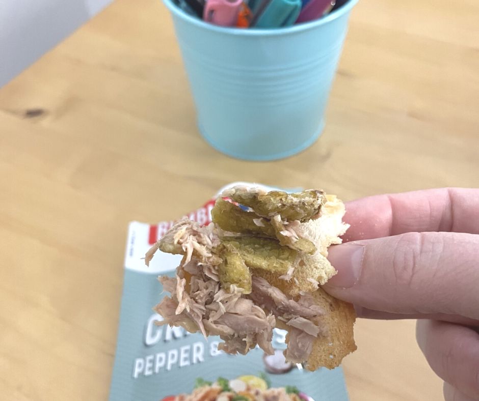 woman eating bagel chip with spicy tuna snack from Dollar Tree at desk