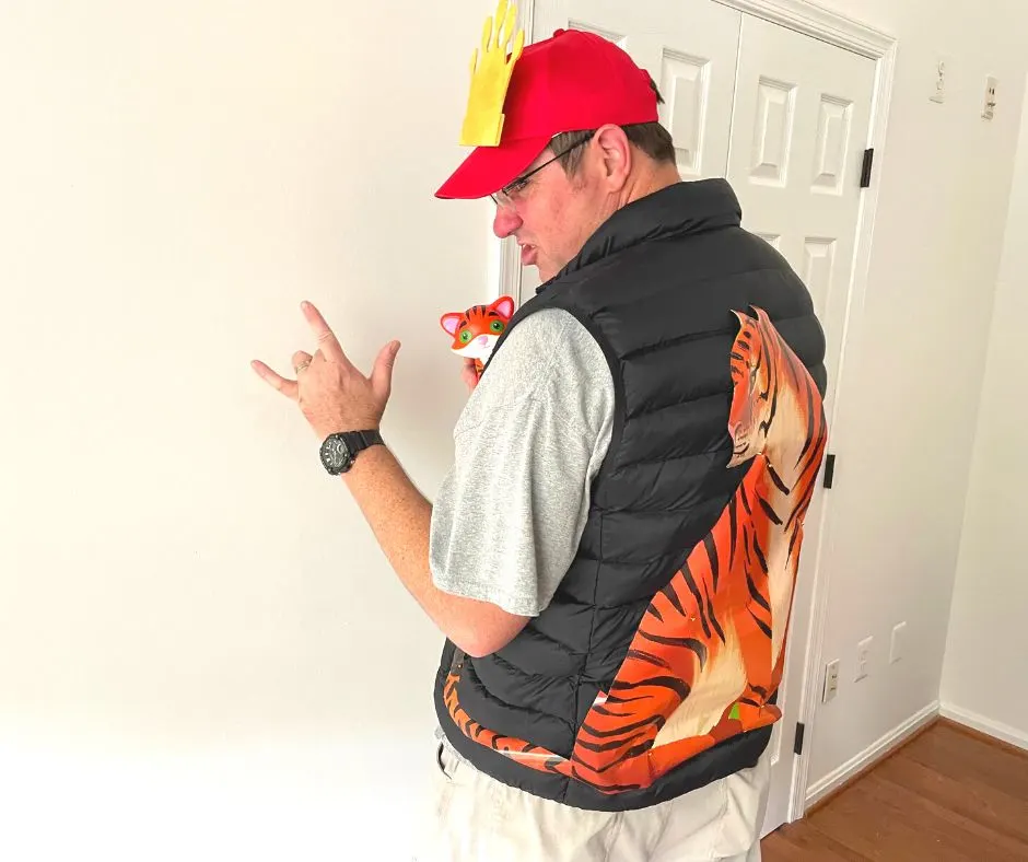 Tiger King costume from Dollar Tree on man, with red hat, crown, tiger on back of black shirt, tiger stuffed animal