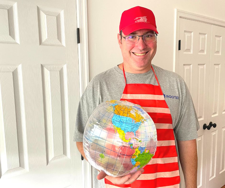 man in red hat, red apron with stripes across it, holding an inflatable globe