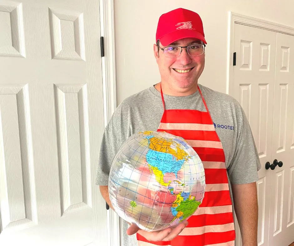 man in red hat, red apron with stripes across it, holding an inflatable globe
