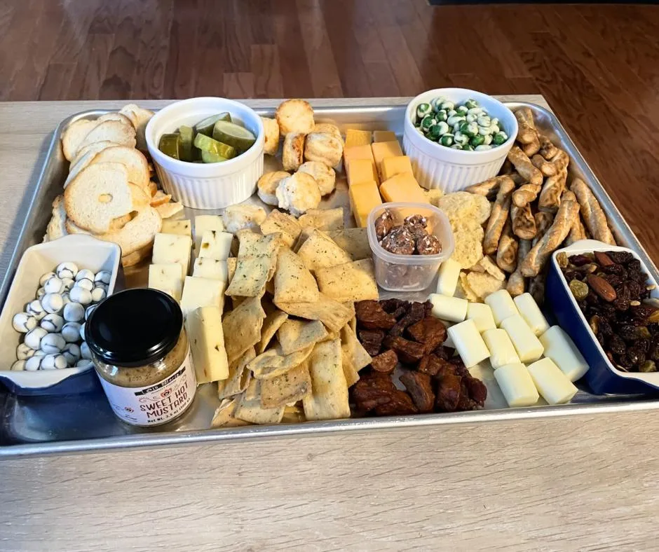 half sheet metal tray filled with food to make charcuterie from dollar tree, like wasabi peas, pepperjack cheese, bagel chips, sweet hot mustard, and more