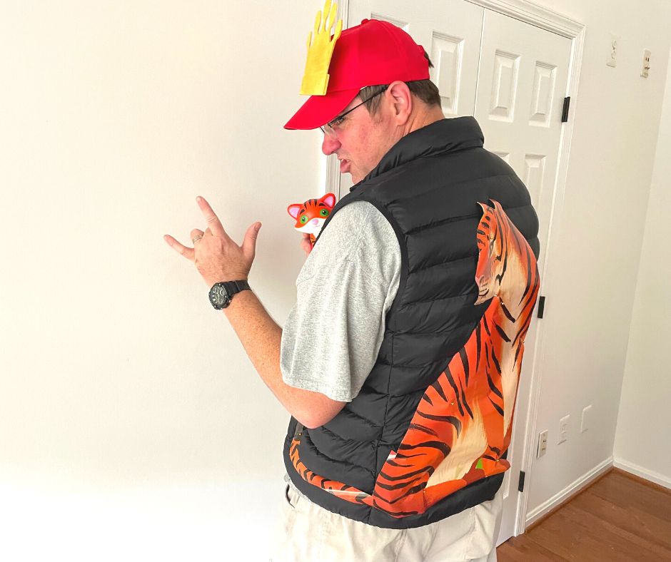 man with stuffed tiger and red hat with golden crown, black vest with big tiger cutout on back