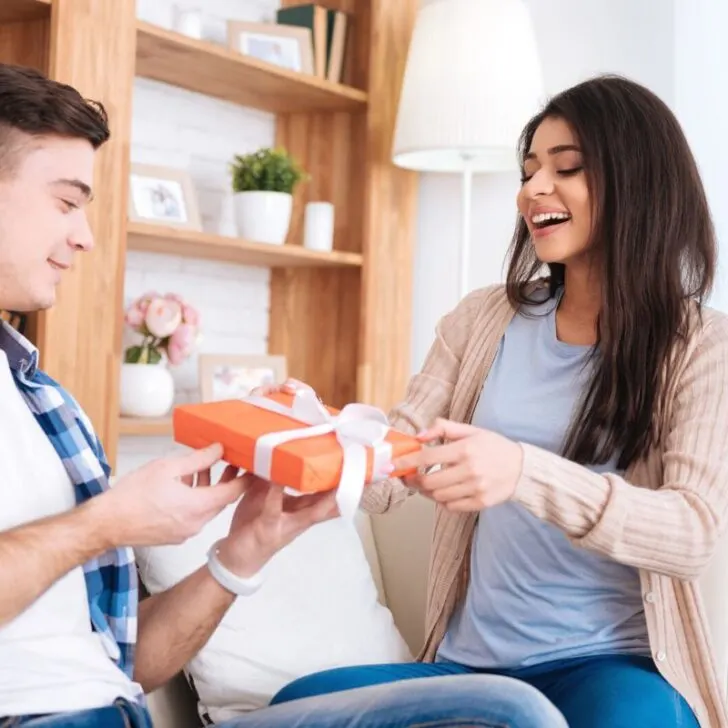 woman handing red gift wrapped box to man in plaid shirt