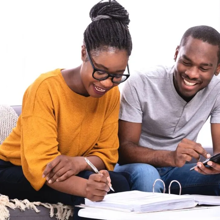 couple on couch smiling working on finances in binder