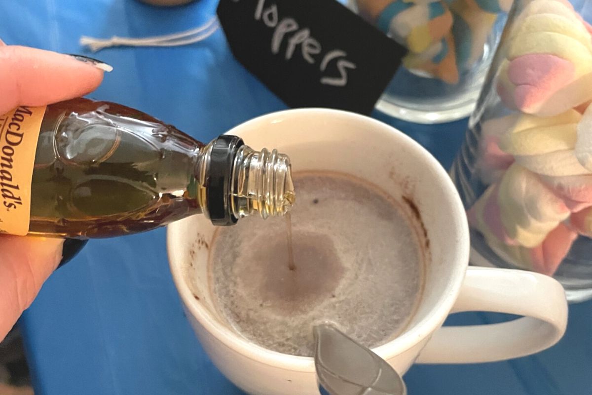 person pouring in maple syrup into hot cup of hot chocolate