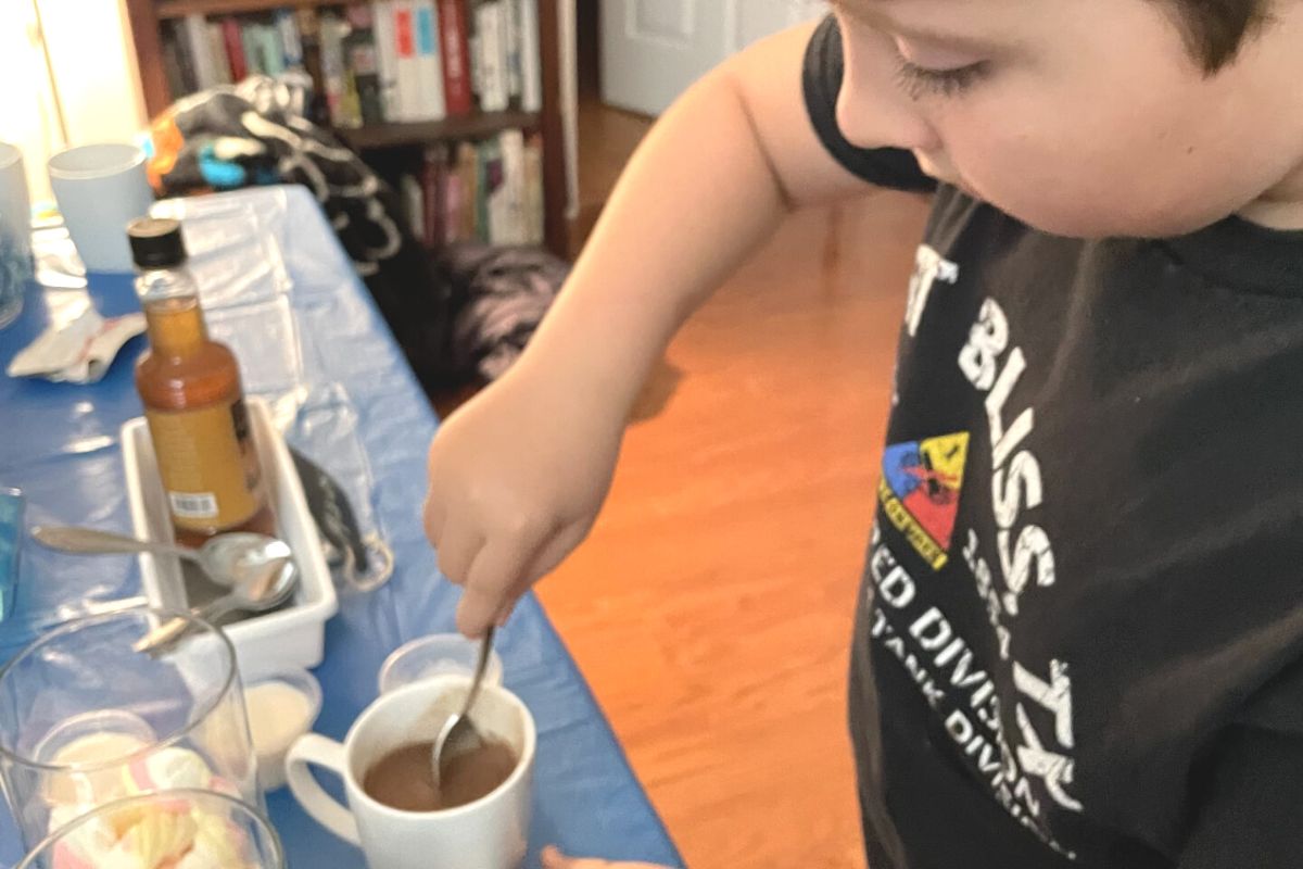 boy stirring the maple syrup around in the cup of hot cocoa