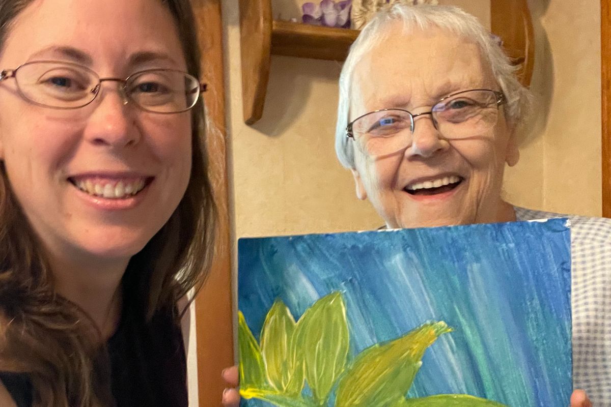 grandmother and author smiling holding up painting with blue background and yellow sunflower