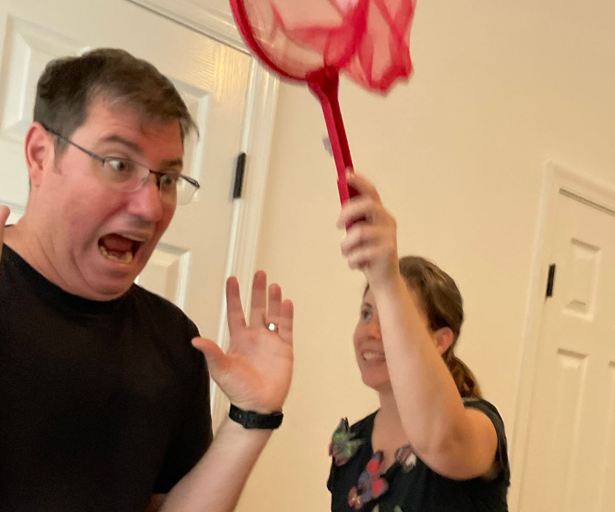 wife with butterflies on shirt pretending to capture husband with butterfly net