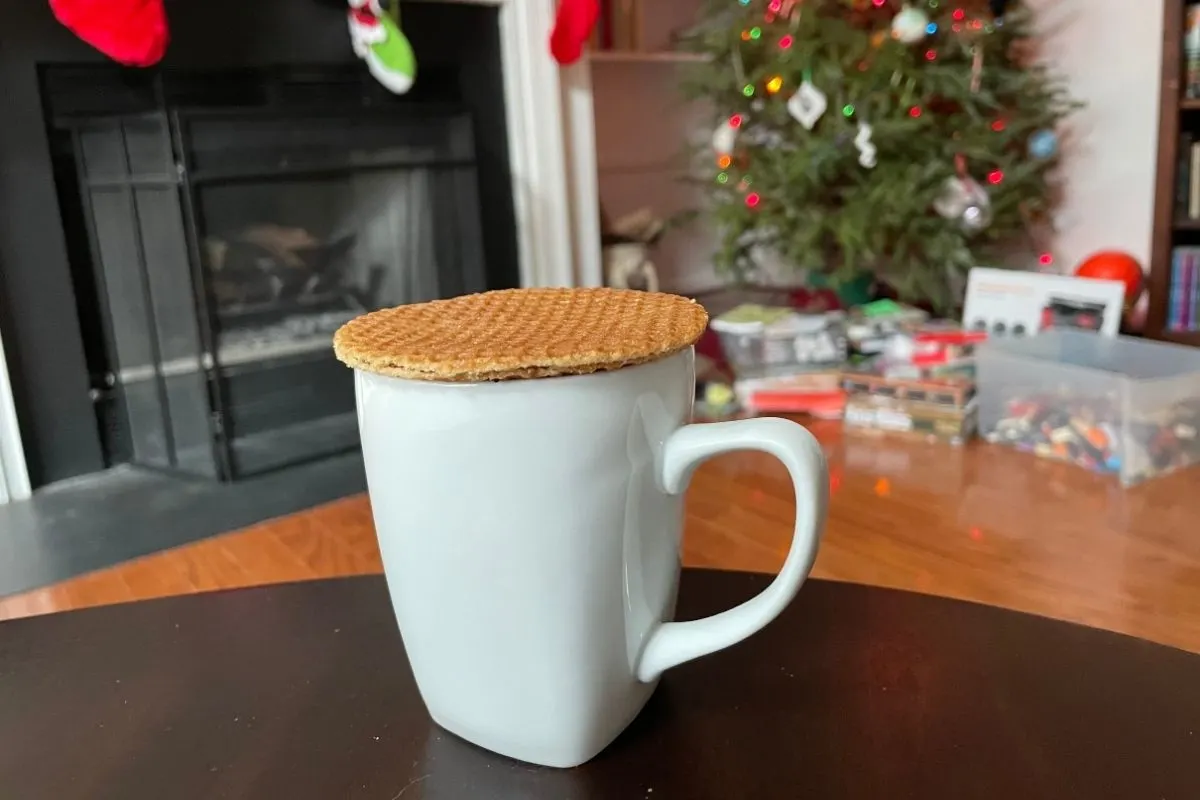 white mug with stroopwafel cookie on top, fireplace and Christmas tree in background
