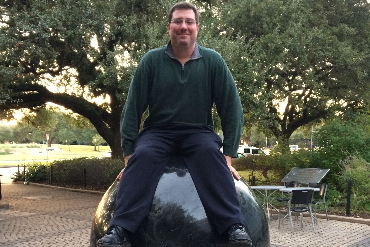 author's husband on top of huge marble world in front of museum for date night