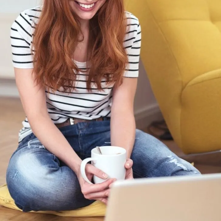 woman in striped shirt on floor, smiling at laptop