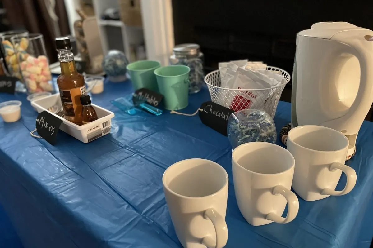 table with blue tablecloth, filled with hot chocolates, toppers, treats, electric water kettle, mugs, etc.