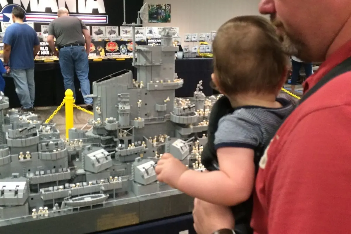 daddy wearing baby in front of ginormous Lego navy ship