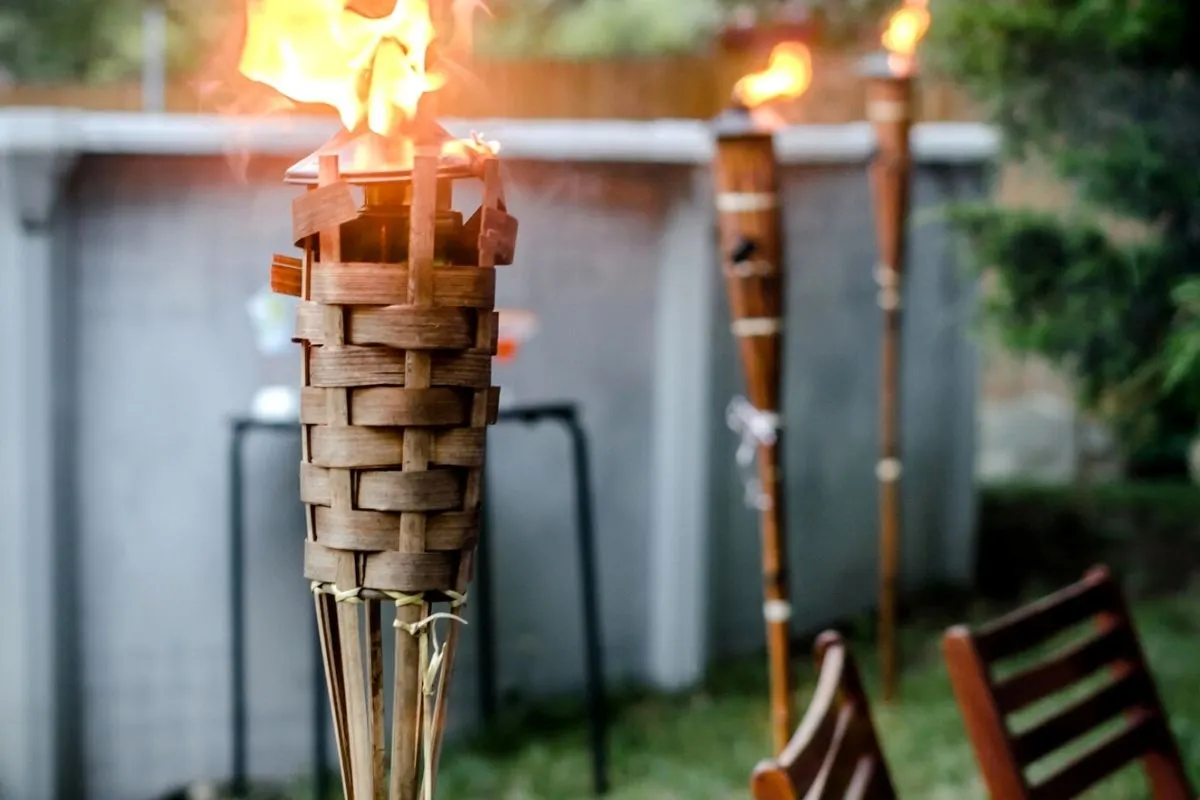 three tiki torches lit, behind chairs and a table in backyard