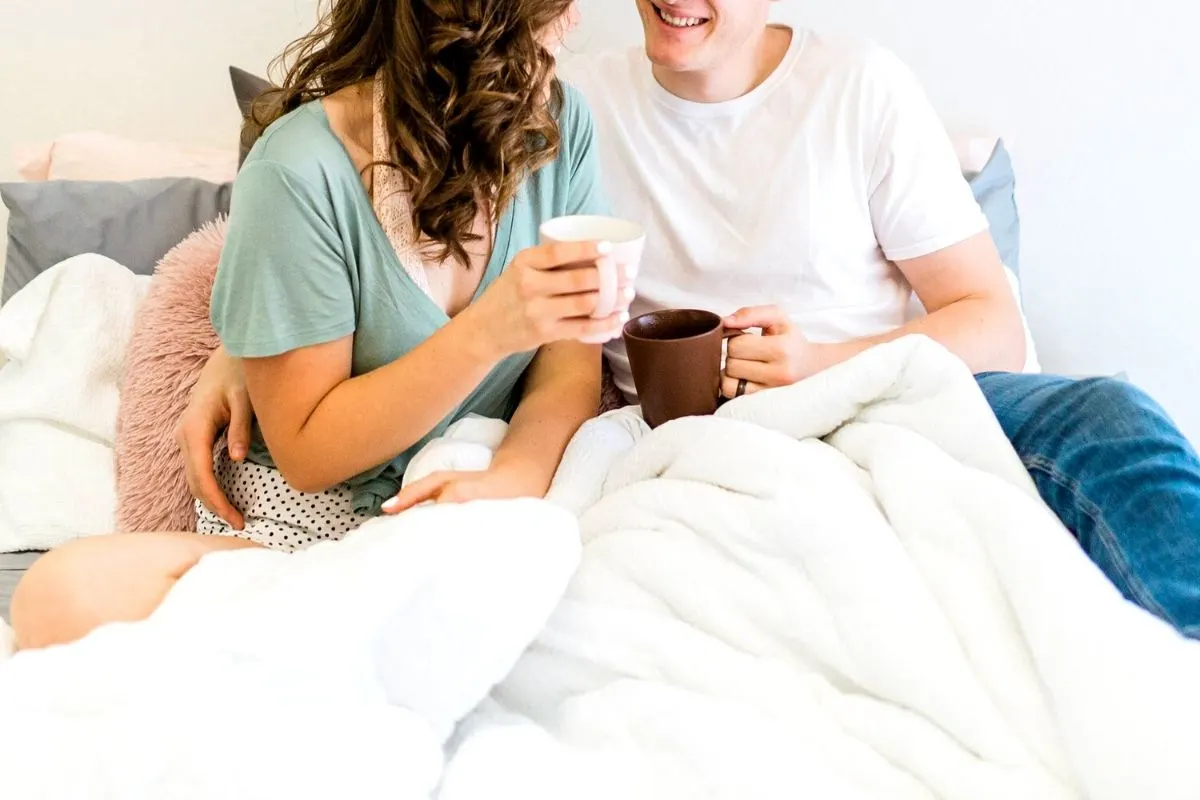 couple smiling in bed, snuggling with cups of coffee