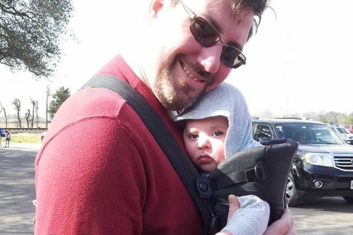 Daddy with baby bjorn, snuggling baby and smiling