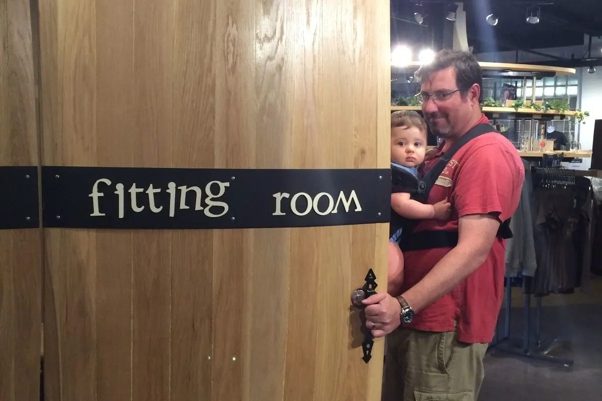 husband opening large door that says "fitting room" while wearing baby and looking at wife lovingly