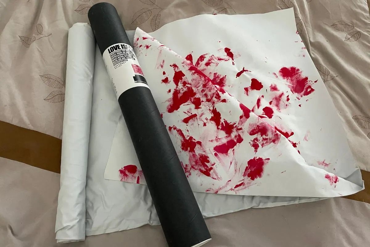 Love is Art black tube on bed, with partly shown canvas showing their Love Art with red/pink paint