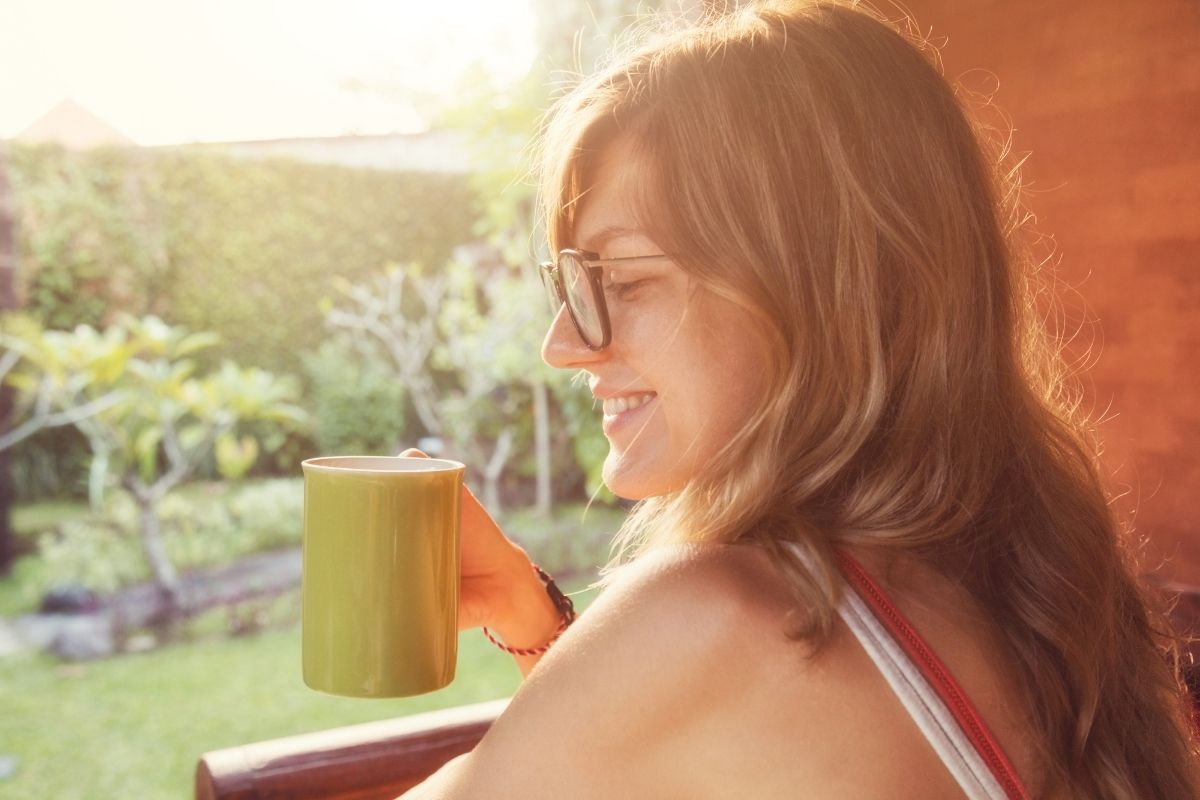 woman in tank top smiling with glasses drinking coffee, on back porch