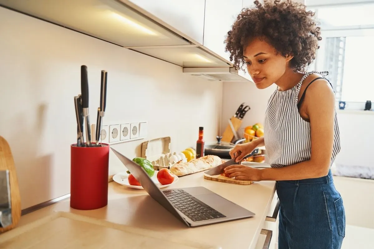 young woman looking at laptop screen while chopping in the kitchen