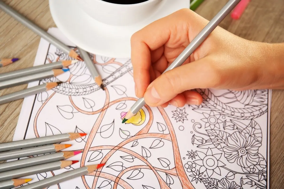 woman coloring mandala adult coloring page on table with coffee