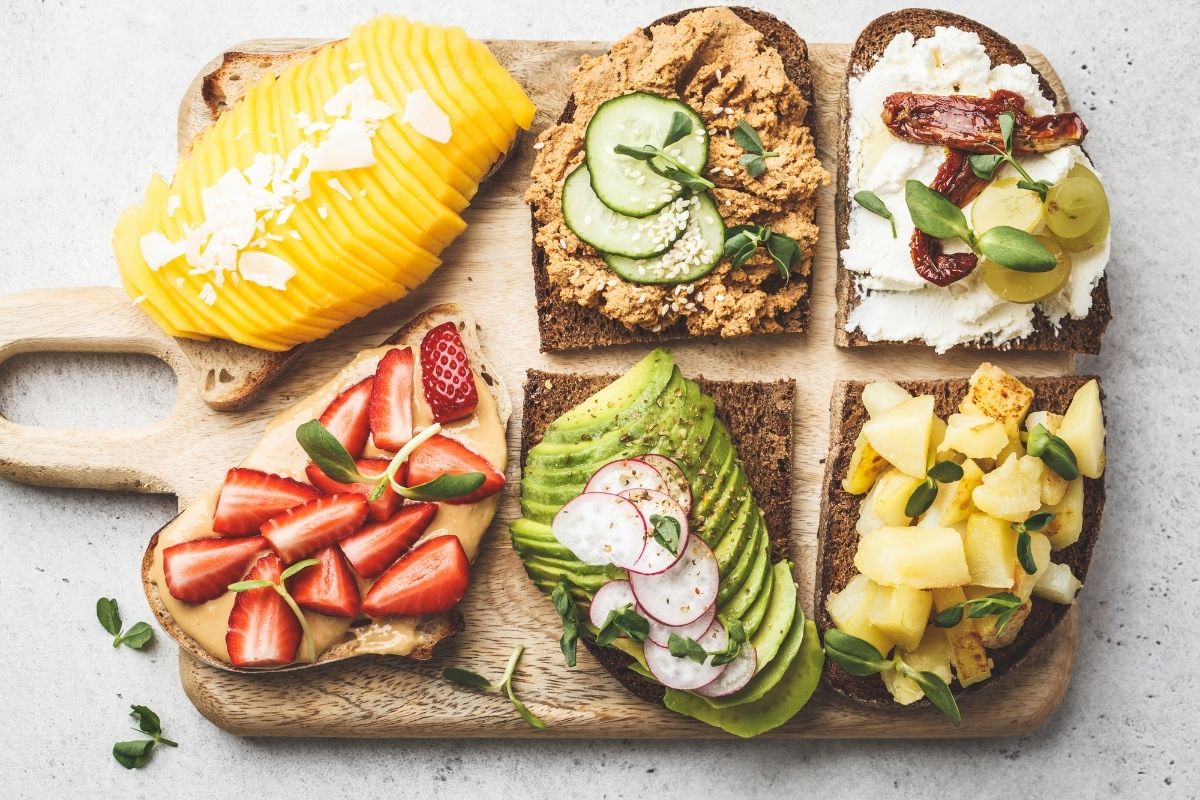 wooden cutting board with six different colorful avocado toasts on top