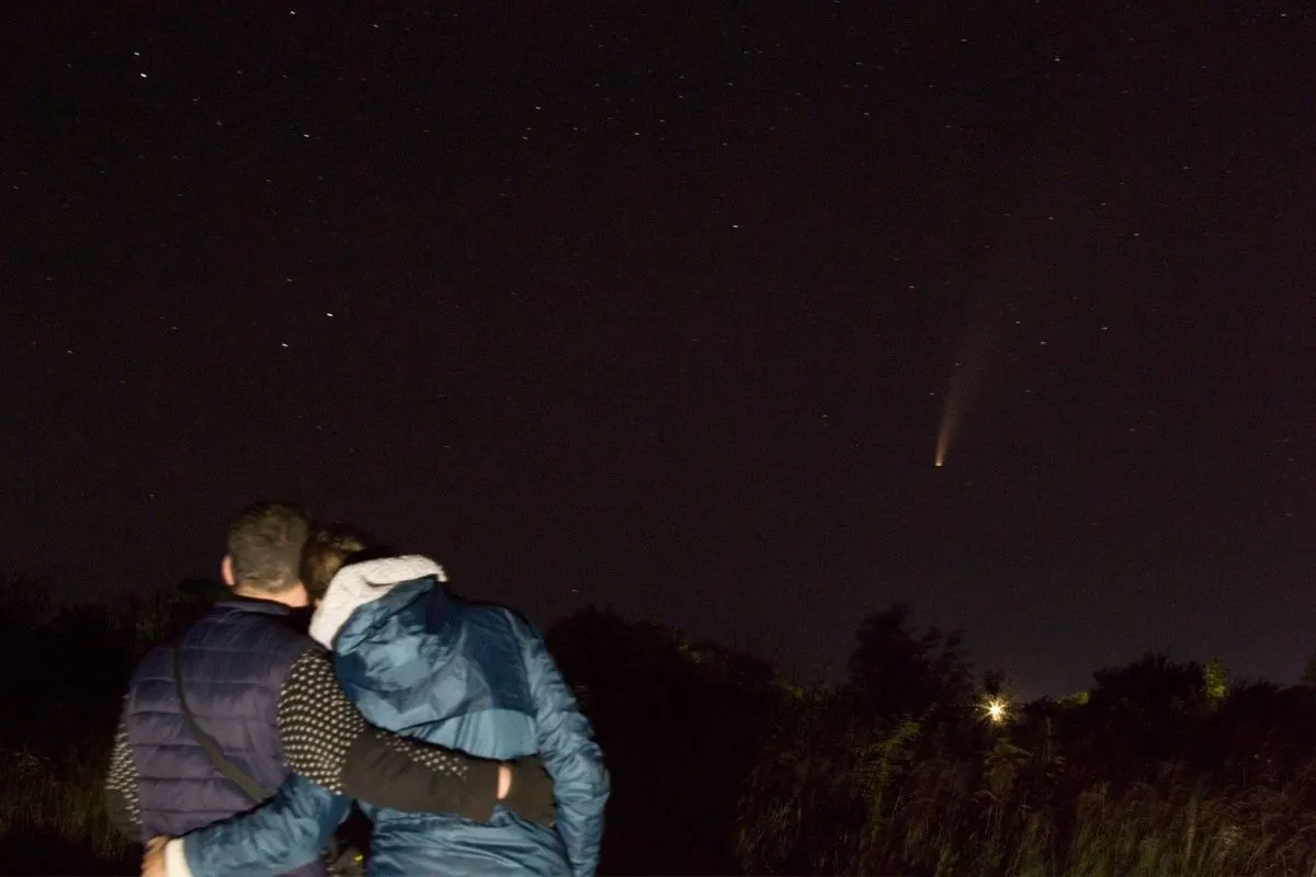 couple in backyard with arms around each other, watching a comet