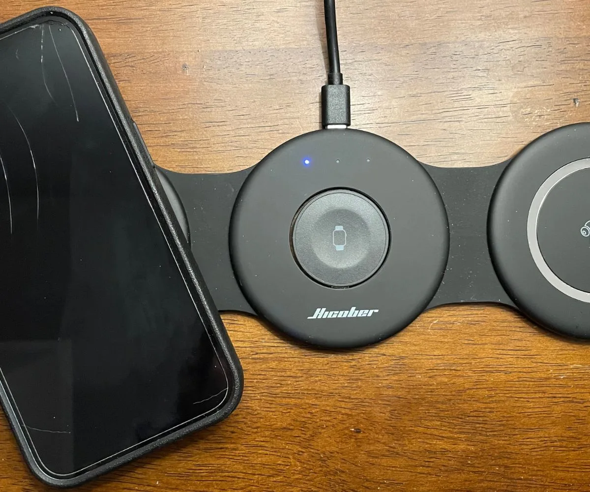black three-pad wireless charger with iPhone on one of the pads, charging