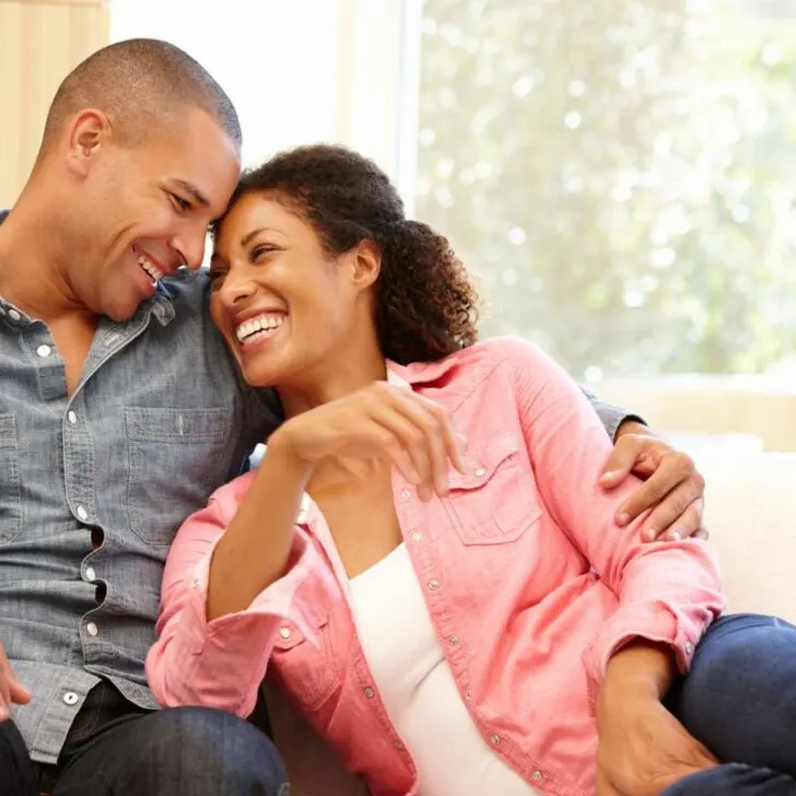couple smiling vibrantly on couch, sharing
