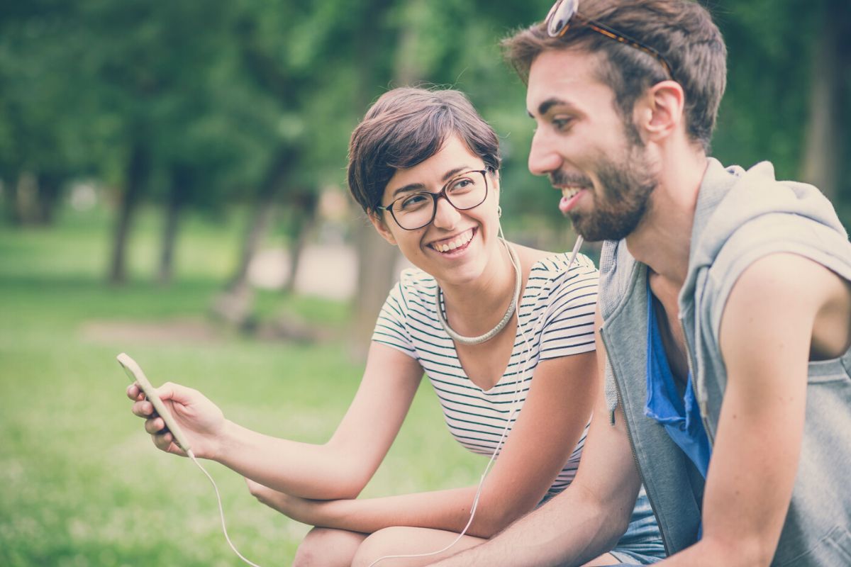 couple on park bench listening to crime podcast having fun and making faces