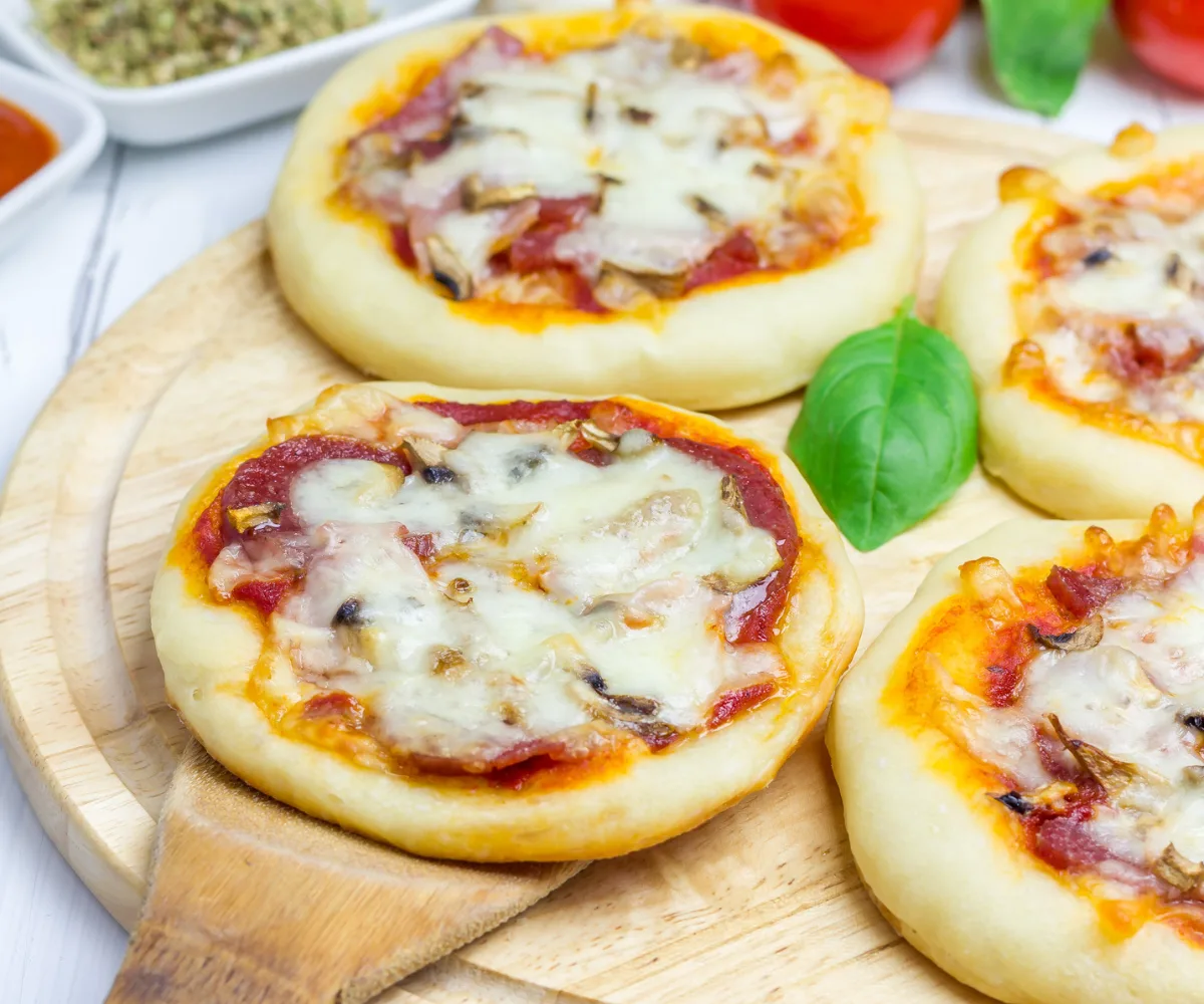 four mini pita pizzas with cheese and sauce on wooden cutting board