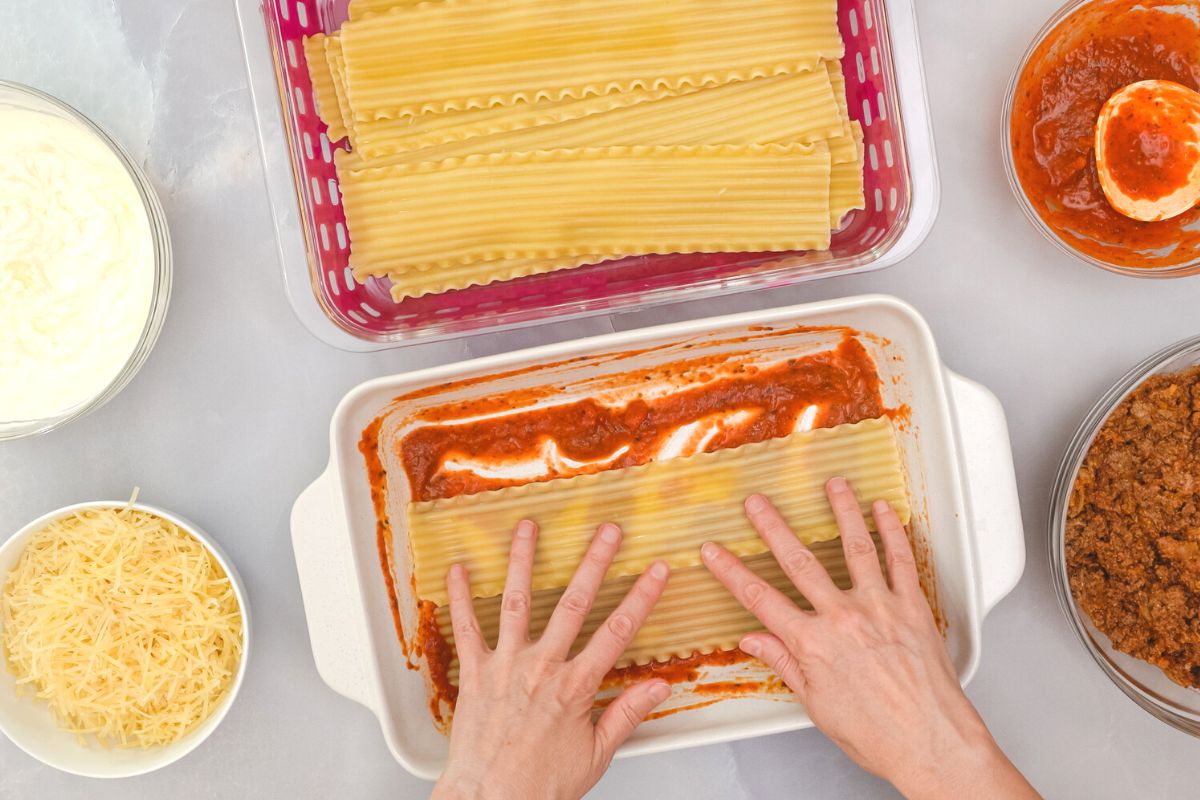 hands preparing two big pans of lasagna