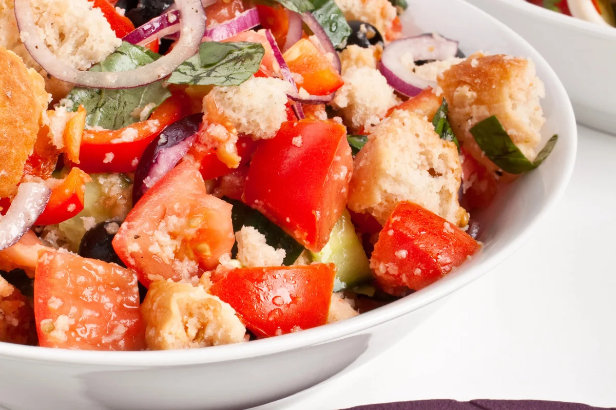 white bowl filled with panzanella salad - bread, tomatoes, sausage, etc. 