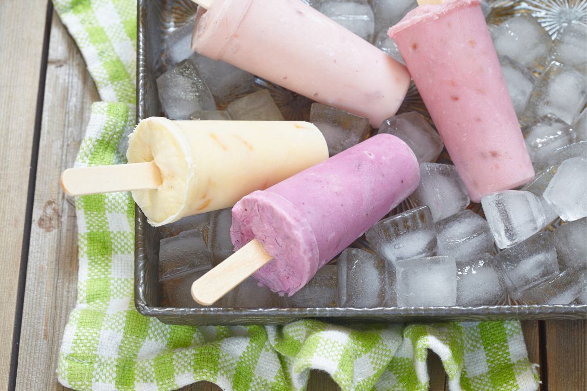 three boozy popsicles in a bucket of ice on wooden table outside