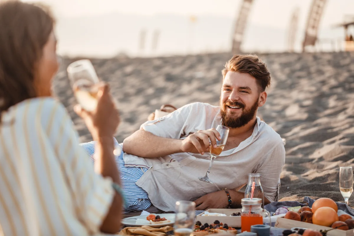 summer charcuterie picnic on beach with wine and couple smiling