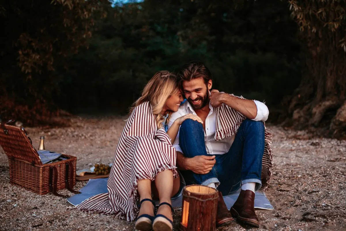 couple snuggling and smiling on picnic blanket at park after dark