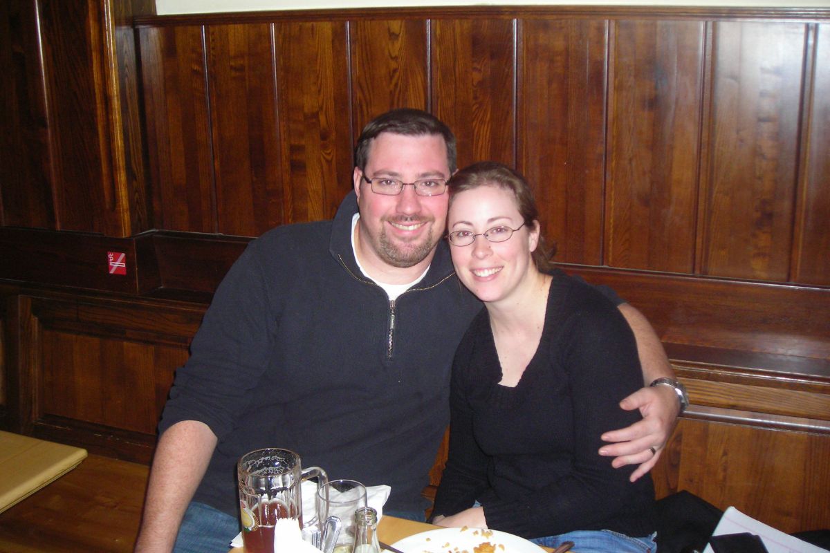 author and husband on honeymoon in pub with wooden background, arms wrapped around each other