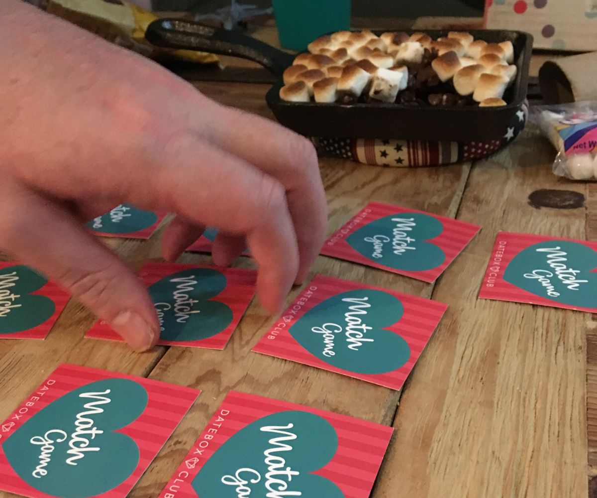 author's husband taking turn playing match love game with skillet s'mores in background