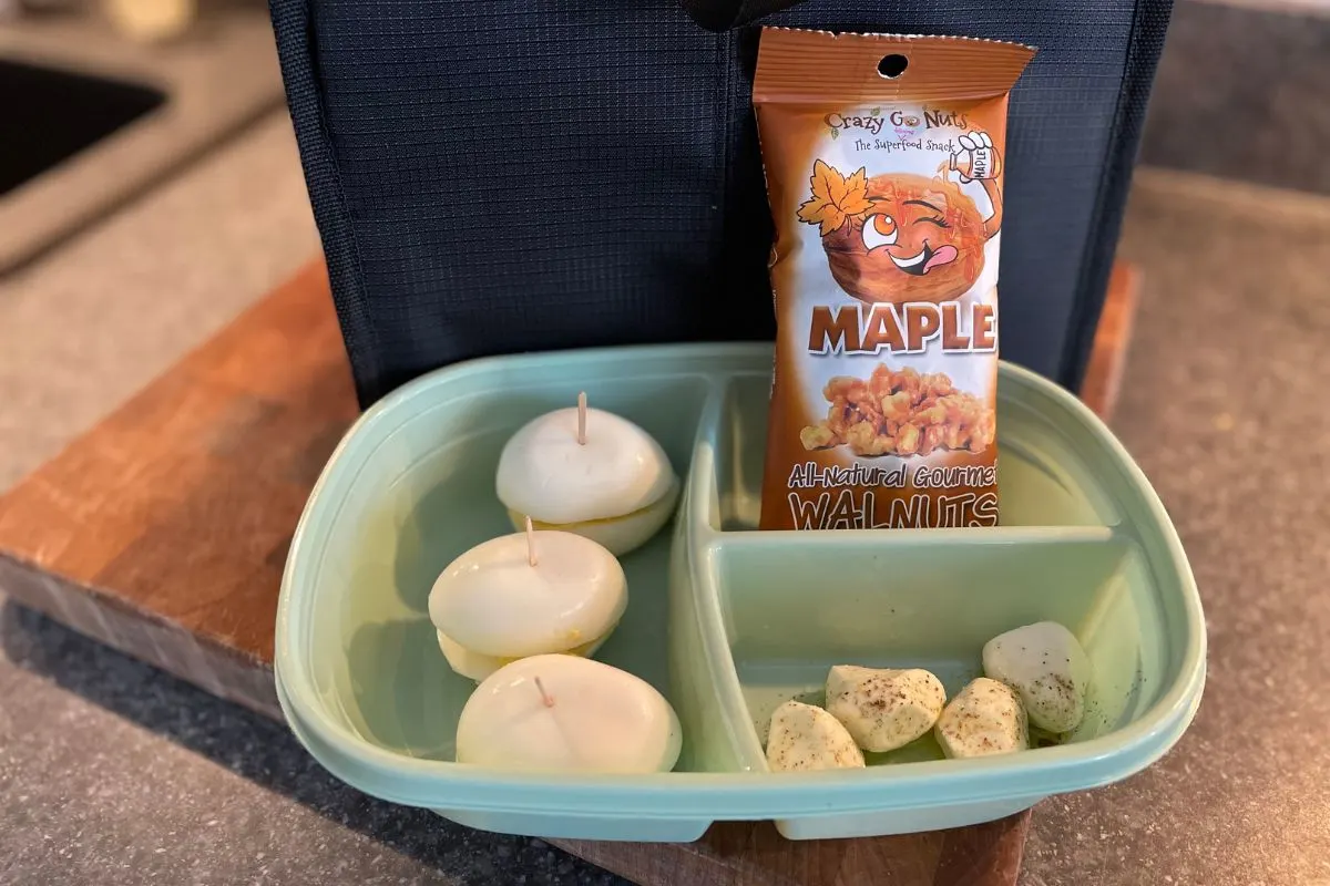 three devilled egg "sandwiches" with toothpicks through each half, mozzarella balls with pepper and olive oil, and package of maple walnuts