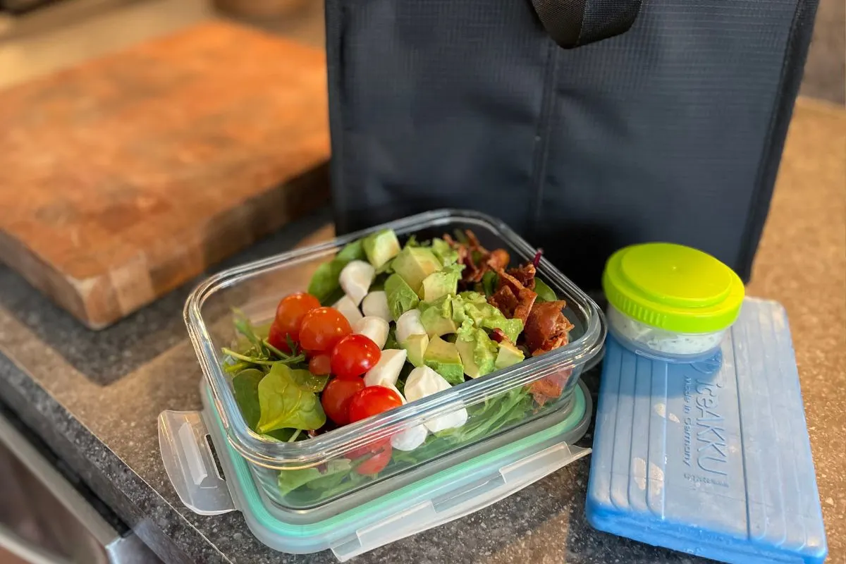 BLT salad in glass container next to black lunch bag, ice cooler, and small container of homemade ranch dressing