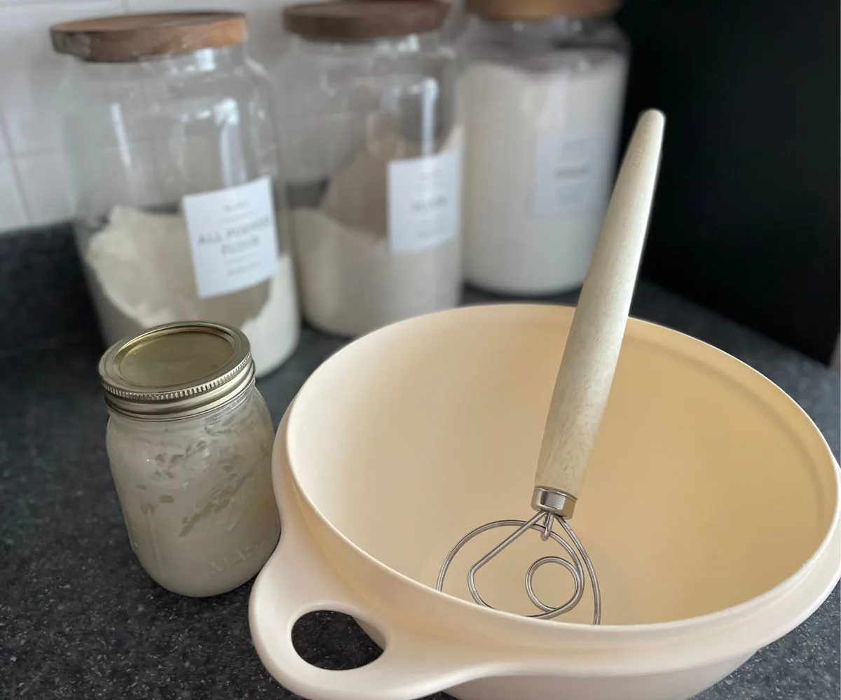 Danish dough whisk sitting in white bowl next to sourdough starter in mason jar